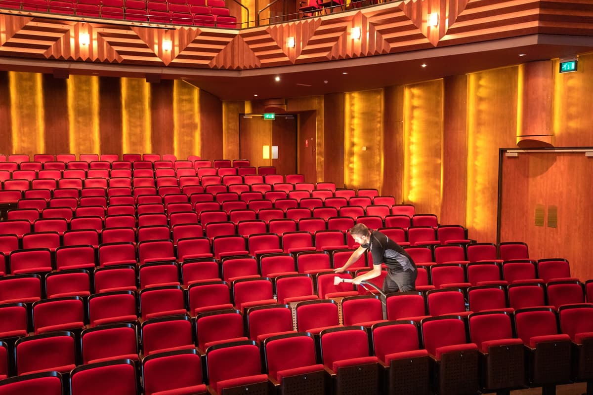 Medewerker reinigt rode theaterstoelen met machine in lege zaal