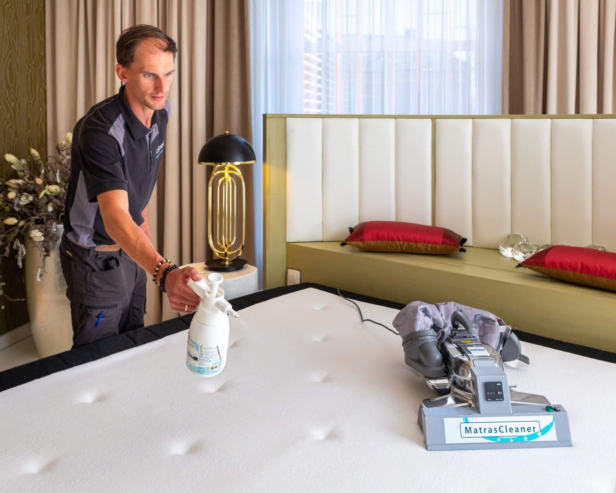Medewerker behandelt een vlek op een matras met reinigingsmiddel naast een matrasreinigingsapparaat